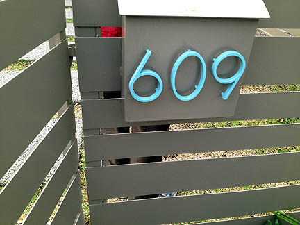 Colorful house numbers pop against this neutral mailbox and fence.