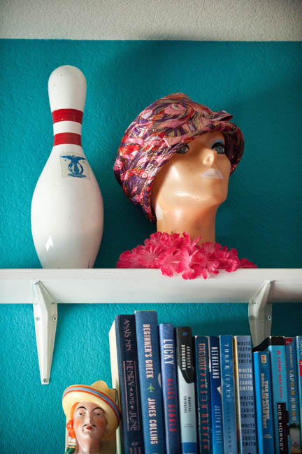 A vintage bowling pin and mannequin head hang out in a teal blue office on white shelves.