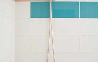 Modern bathroom tile design featuring elongated subway tiles in teal blue, bright orange, taupe-gray, and white, with simple brushed nickel plumbing fixtures.