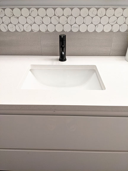 Floating white lacquer double vanity in modern gray bathroom remodel in Austin featuring large white penny accent tile, quartz countertops, and black plumbing fixtures.