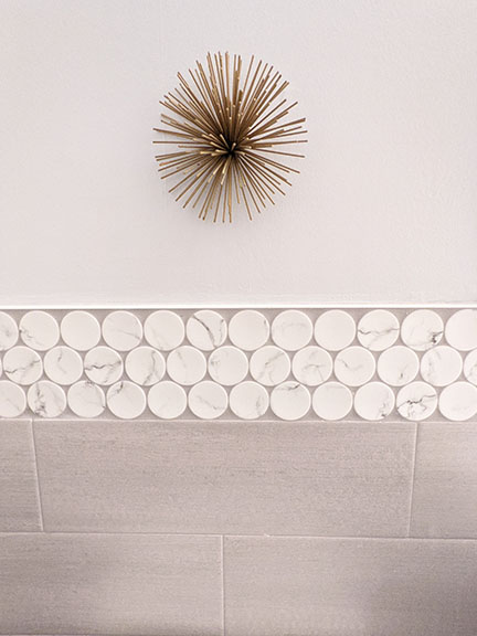 Brass mid-century modern starburst wall art in bathroom remodel featuring large white penny round accent tile in Austin, Tx.