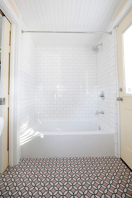 White subway tub surround, butter yellow paint and pale pink mid-century inspired tile floor in train caboose tiny house bathroom in Austin, TX