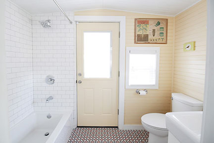 Train caboose tiny house bathroom with butter yellow paint white subway tub surround and pale pink geometric tile floor.