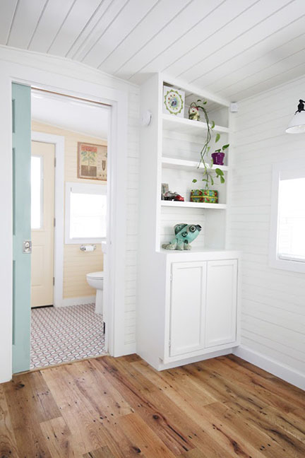 Built-in inside train caboose tiny house kitchen with view of adjoining bathroom's pink white floor tile.