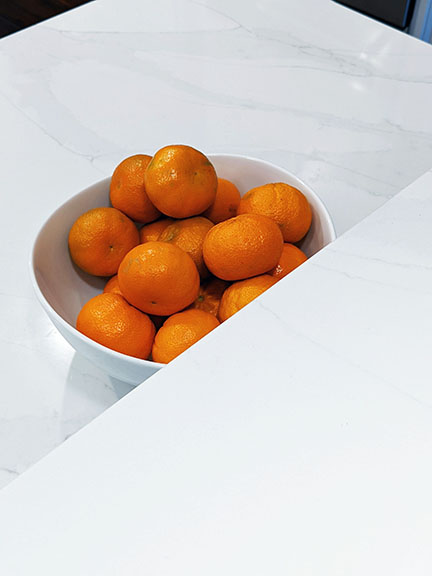 Bowl of orange clementines on white marble quartz countertops.