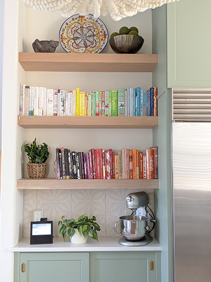 Kitchen remodel featuring cabinets painted SW 6192 Coastal Plain, floating French Oak shelves with rainbow colorized cookbooks, pewter KitchenAid mixer