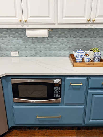 Undercabinet microwave featuring a child-lock device, surrounded by white and blue cabinetry, mid-century inspired tile backsplash and white marble quartz countertops.