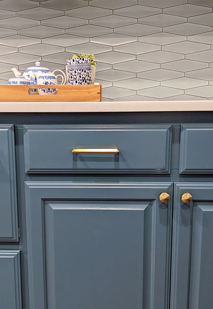 Detail view of brushed brass hardware on blue painted cabinets and mid-century modern tile backsplash