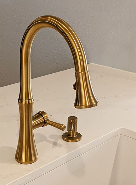 Brushed brass kitchen sink faucet and built-in soap dispenser on quartz marble countertops.